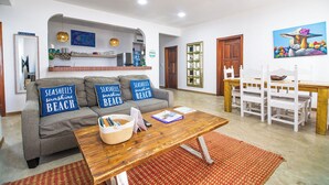 A living room with a sofa, a coffee table, a dining table with chairs, a kitchen area, and a painting on the wall. - 4 br/ Oceanview/Pool/Walk to Centar of San Pedro (San Pedro)