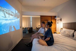 A hotel room with a bed, a TV screen displaying a snowy landscape, a wooden headboard, and a nightstand with a lamp. - Princes Wharf Penthouse (Auckland Central)