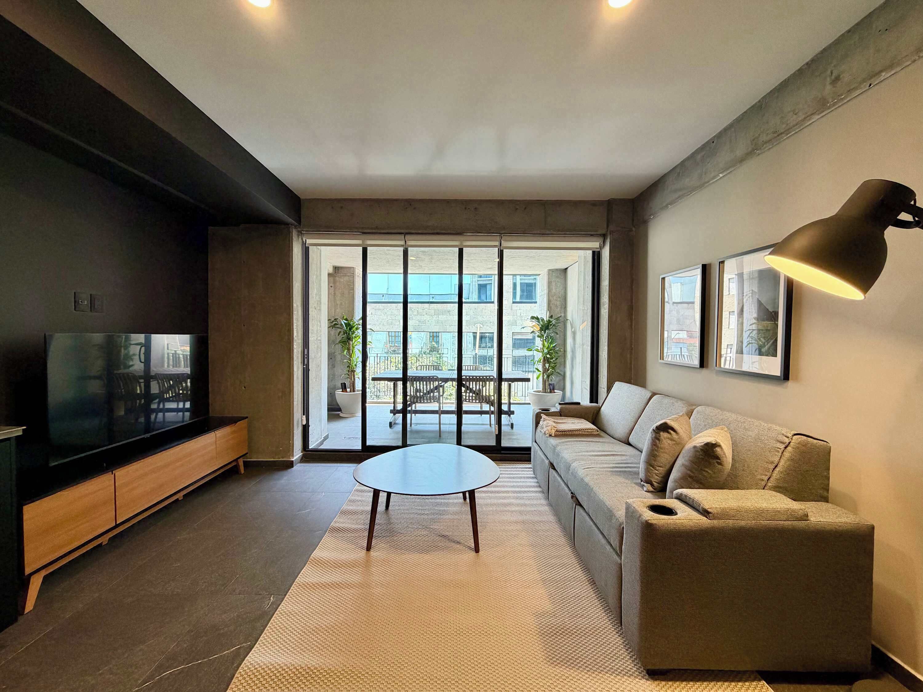 Uma sala de estar moderna com sofá, mesa de centro, televisão e varanda com plantas.