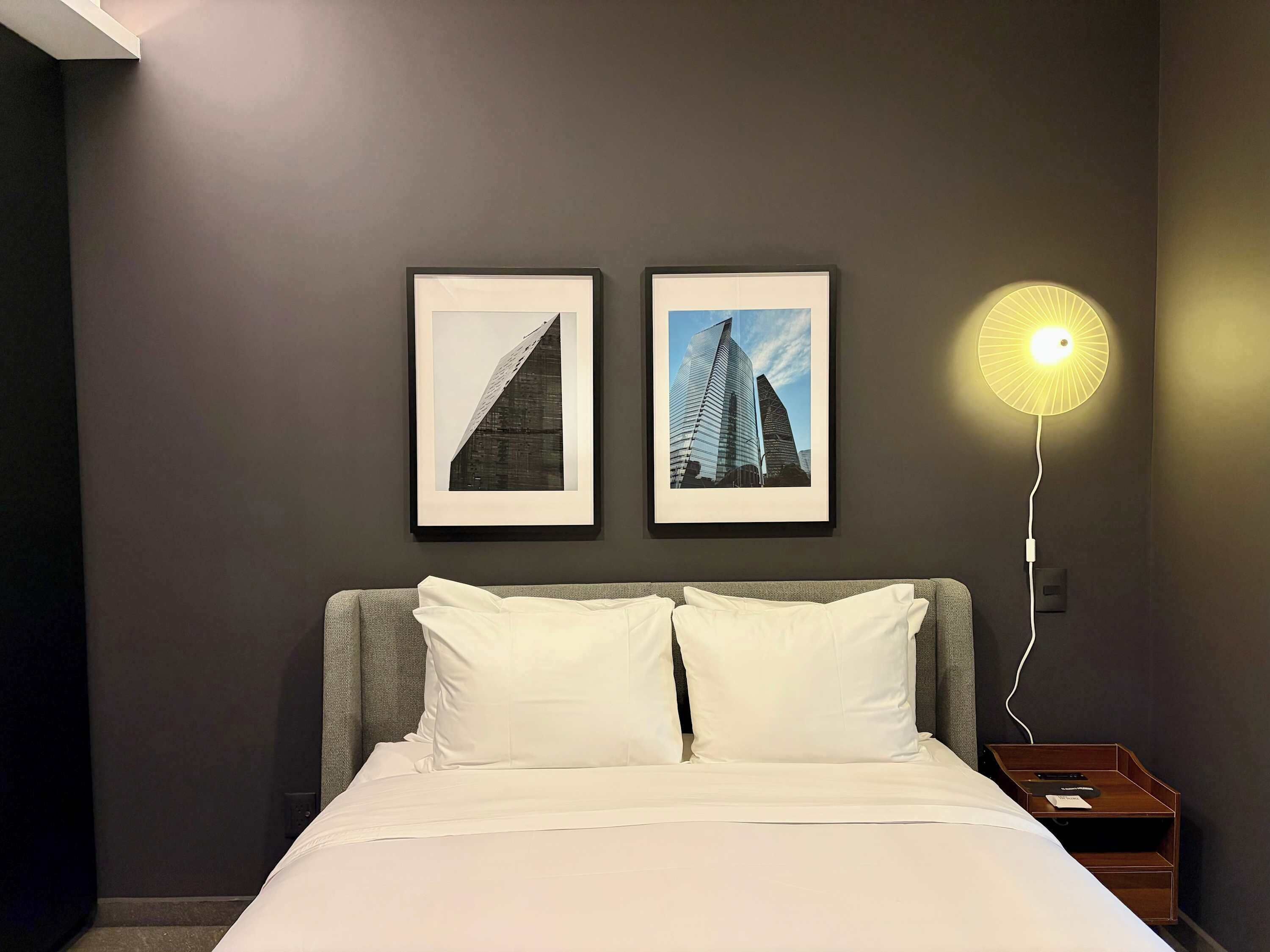 Een hotelkamer met een bed, twee foto's in lijsten aan de muur en een bedlampje.