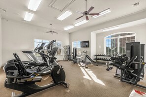 Ein Fitnessstudio mit Trainingsgeräten, großen Fenstern und einem Deckenventilator.
