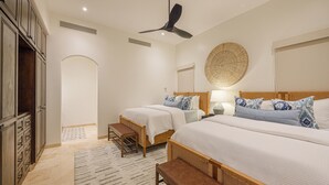 Un dormitorio con dos camas, ventilador de techo, mesita de noche, lámpara y decoración de pared tejida.