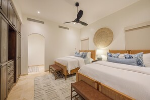 Ein Schlafzimmer mit zwei Betten, einem Deckenventilator, einem Nachttisch, einer Lampe und einer Wanddekoration aus Gewebe.