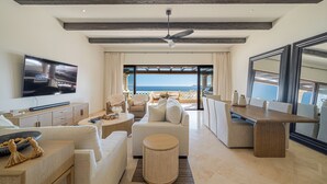 Amplia sala de estar con televisor de pantalla plana, ventilador de techo, mesa de comedor y vista al océano.