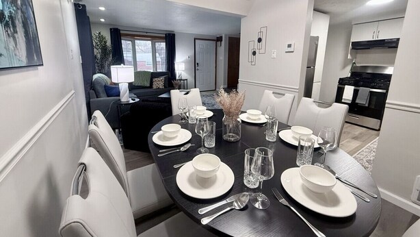 Un comedor con una mesa redonda dispuesta para cuatro, sillas blancas y una cocina moderna al fondo.