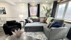Una sala de estar moderna con un sofá seccional gris, un sillón negro, una mesita auxiliar y un jarrón con plantas secas.