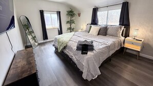 Un dormitorio con cama, mesitas de noche, un espejo, una planta y una ventana.
