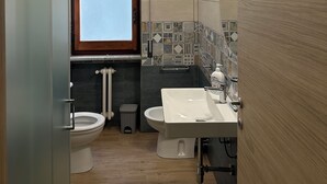 Ein modernes Badezimmer mit Toilette, Bidet und Waschbecken, einem Fenster und einer gefliesten Rückwand.