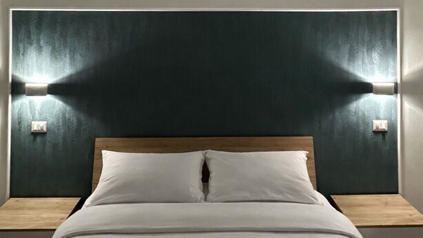 Ein Hotelzimmer mit Bett, Holz-Kopfteil, zwei Nachttischlampen und einer Wand-Klimaanlage.