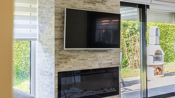 Una sala moderna con chimenea de piedra, televisor de pantalla plana y un patio con parrilla.