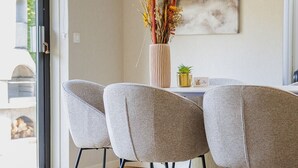 Un comedor con una mesa moderna, tres sillas grises, un florero con flores secas y un cuadro en la pared.
