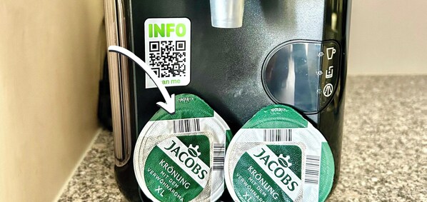 En kaffemaskine med en QR-kode og to kaffekapsler mærket 'Jacobs'.