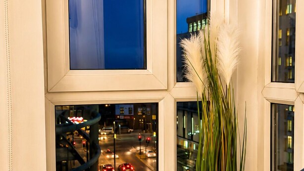 Une fenêtre donnant sur une rue animée la nuit, une porte blanche et une plante dans un panier tressé.
