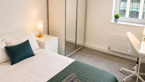Une chambre d’hôtel équipée d’un lit, d’une armoire, d’un bureau et d’une fenêtre donnant sur des immeubles.