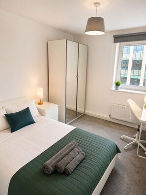 A hotel room with a bed, a wardrobe, a desk, and a window with a view of buildings. - Spacious 3-Bedroom Flat in Central Leeds (Leeds)