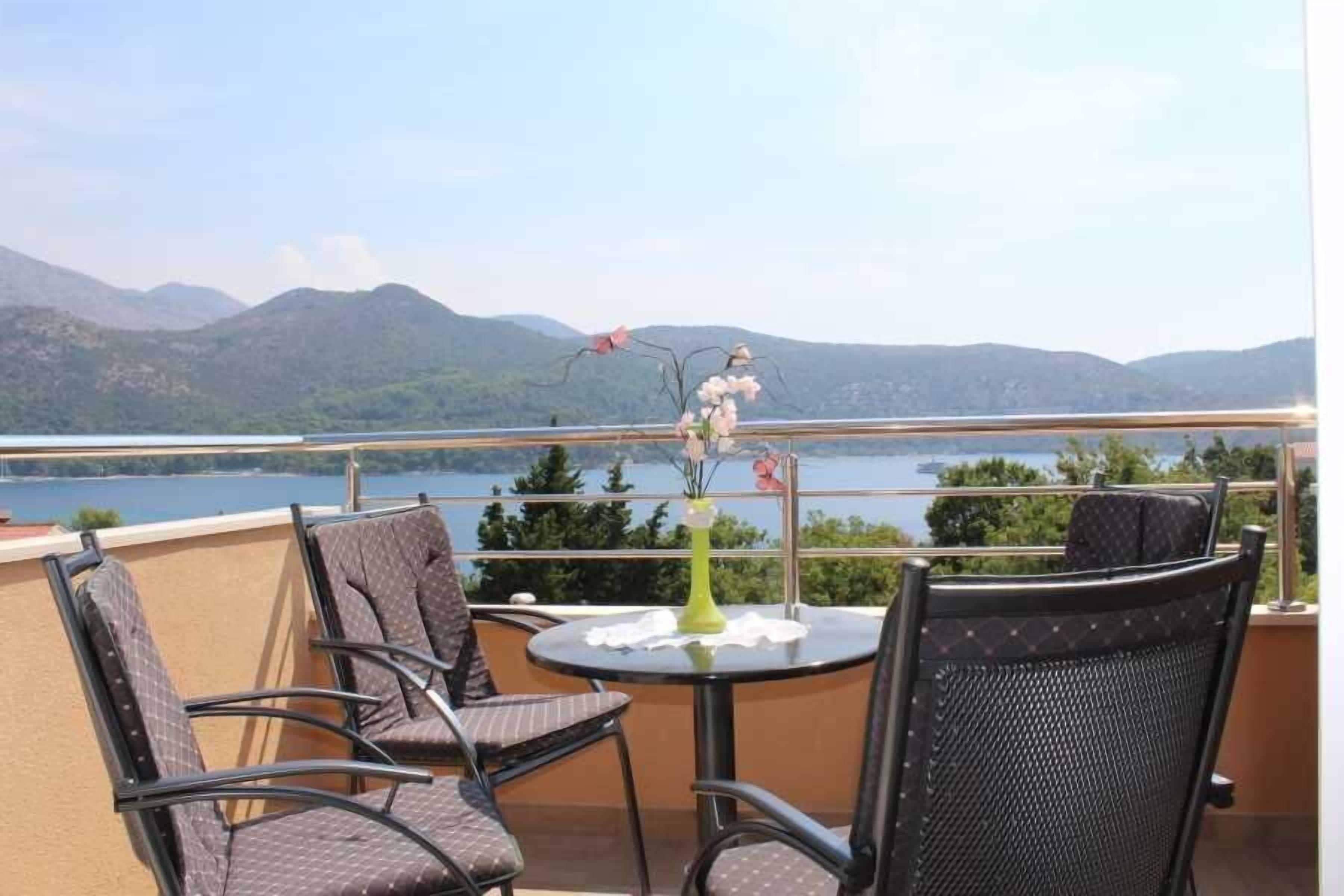 A balcony with chairs and a table, overlooking a lake and mountains.