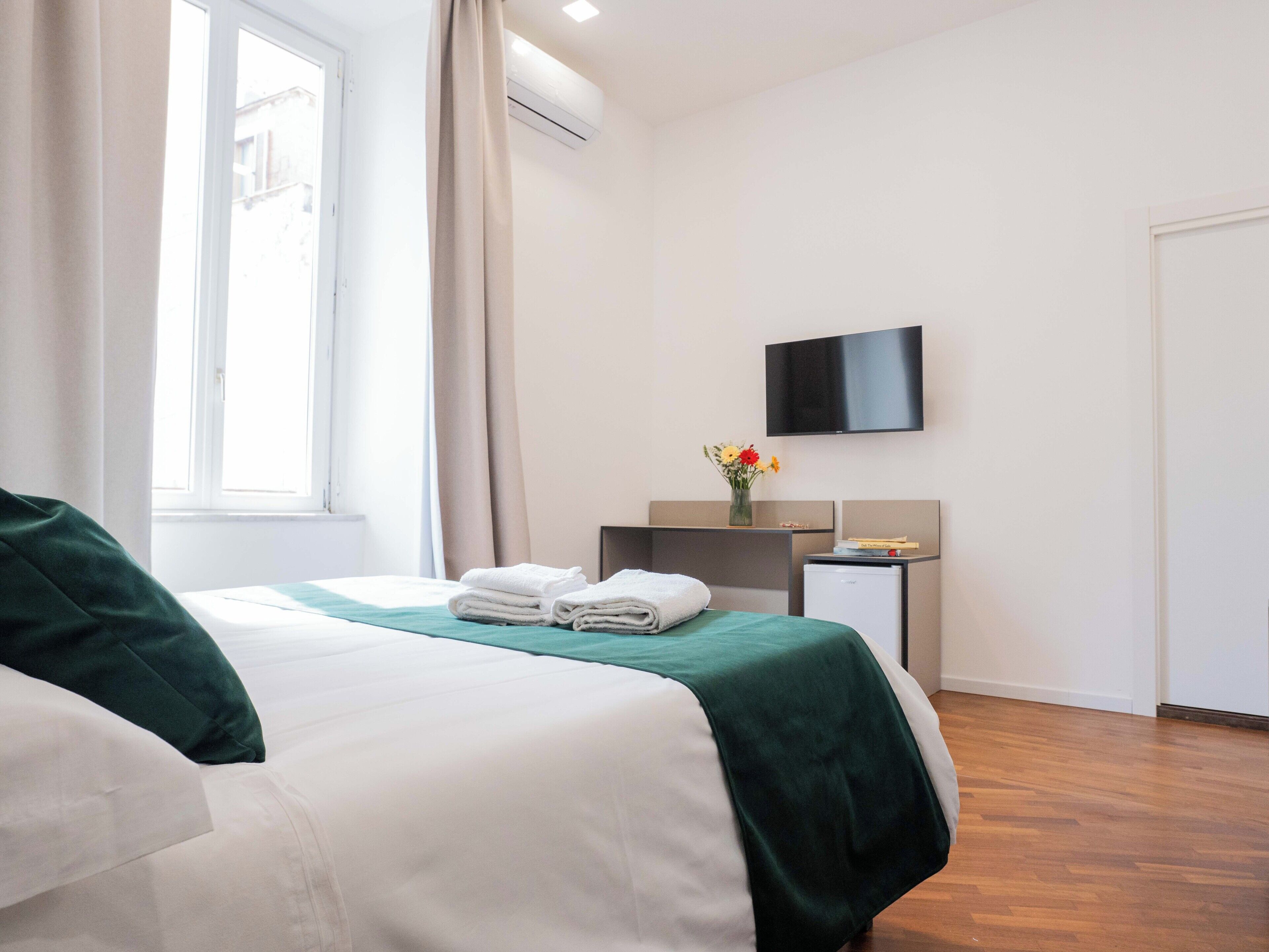 A hotel room with a bed, a desk, a TV, and a window.