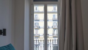 Una habitación con cama, ventana con vistas a balcones y cortina.
