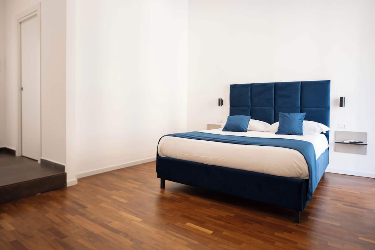 A bedroom with a bed, wooden flooring, a door, and a wall-mounted light.