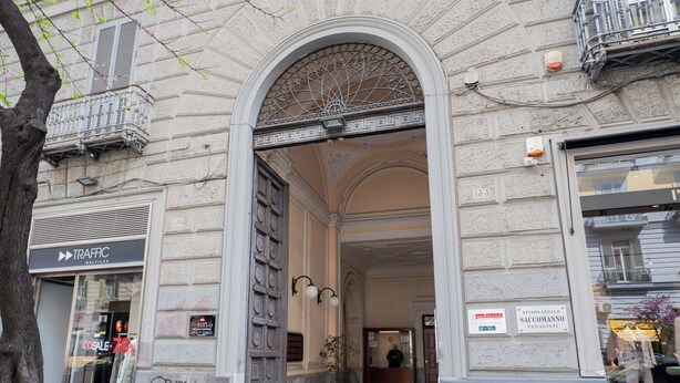 Una entrada a un edificio con un amplio arco, un letrero que dice 'Studio Legale Saccomanno Penalisti' y una tienda 'Traffic Multilab' a la izquierda.