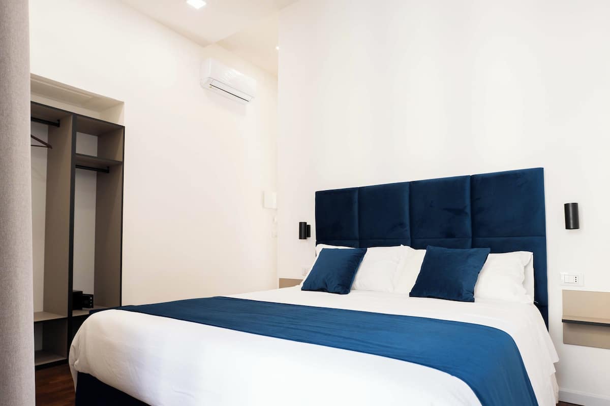 A modern hotel room with a bed, a wardrobe, and a wall-mounted air conditioning unit.