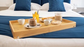 Una bandeja de desayuno bien dispuesta sobre una cama con cabecera azul, almohadas blancas y pared blanca.