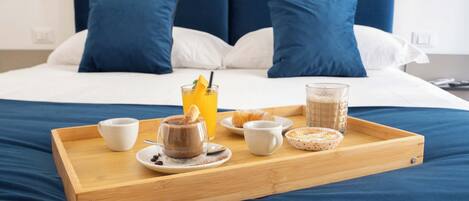 A neatly made breakfast tray on a bed with a blue headboard, white pillows, and a white wall.
