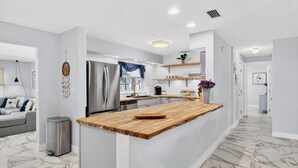 Eine moderne Küche mit Marmorboden, einem Edelstahlkühlschrank und einer Holz-Kochinsel.