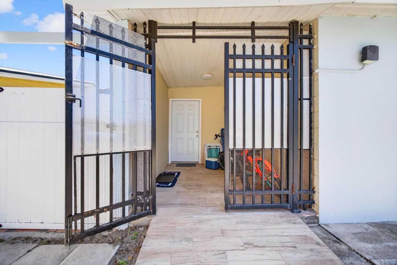 A gated entrance to a property with a door, a small outdoor area with a mat, and a bicycle.