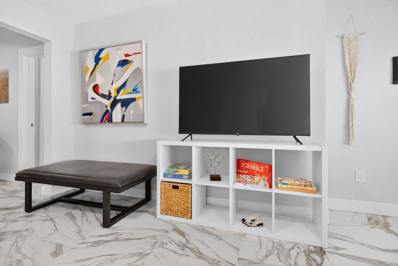 A living room with a TV, a bench, a bookshelf, and a painting.