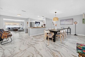 Amplia sala de estar con piso de mármol, una mesa de comedor con sillas, un sofá y una cocina con refrigerador y pileta.