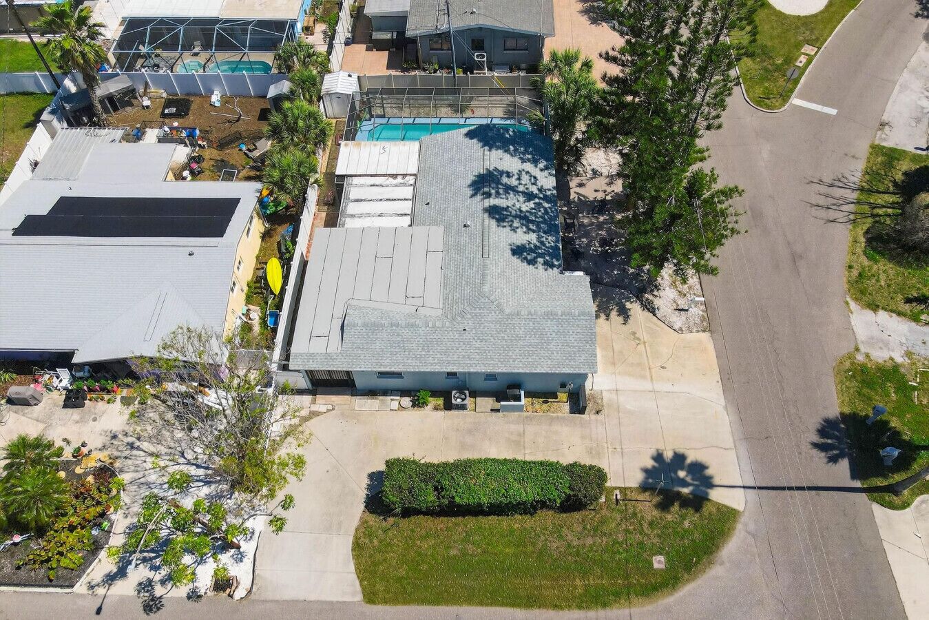 An aerial view of a residential area with a house featuring a sloped roof, a swimming pool, and a well-maintained lawn.