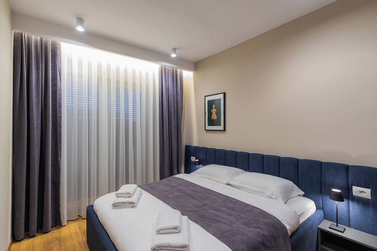 Une chambre d’hôtel avec un lit, des rideaux, une table de chevet, une lampe et un tableau encadré au mur.