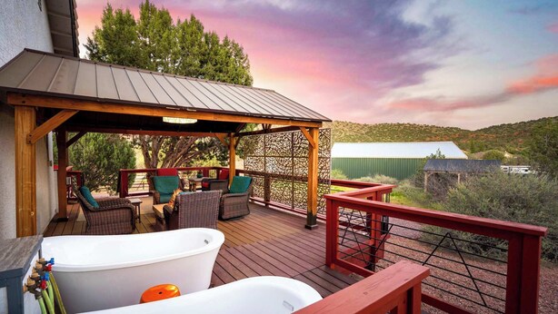 Eine Terrasse mit Gartenmöbeln, einem Whirlpool und Blick auf ein grünes Gebäude im Hintergrund.