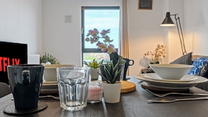 Moderni olohuone, jossa on sohva, koristekasvi pöydällä, televisio ja ikkuna, josta on näkymä.
