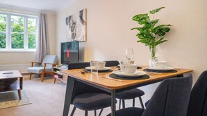 Et spiseområde med et bord dækket til to personer, en potteplante og et fjernsyn i baggrunden.