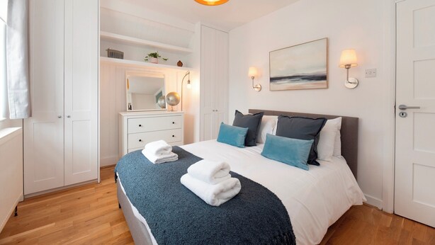 Un dormitorio con cama, armario blanco, mesita de noche, lámpara y una obra de arte en la pared.