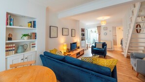 Una sala de estar con un sofá azul, una mesa de madera, una estantería y una escalera.