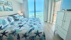 Une chambre avec un grand lit, une télévision, une commode et une vue sur l’océan.