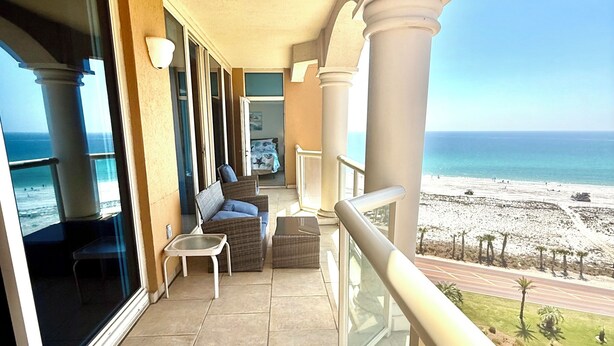 Un balcon avec vue sur la plage, un canapé, une chaise et une table.