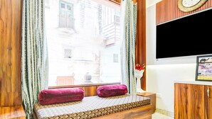 A room with a wooden bench, a TV, and a window with curtains.