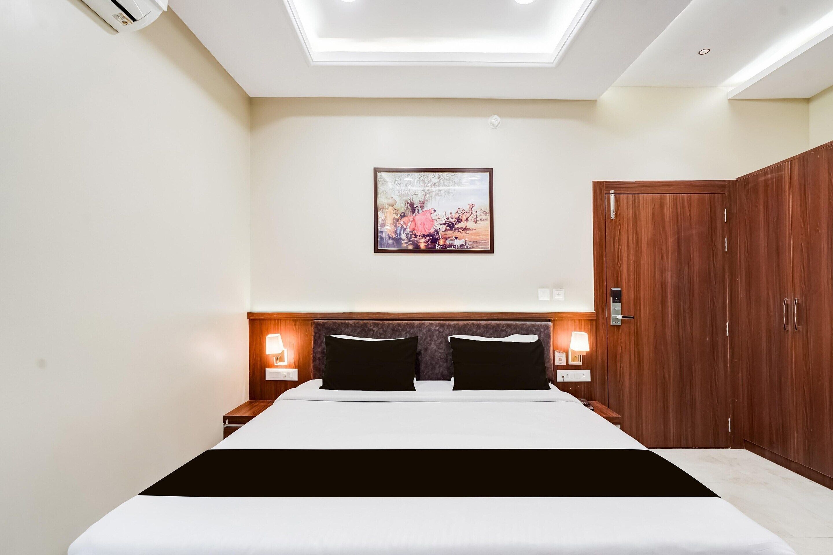 A hotel room with a bed, bedside lamps, a painting on the wall, a wardrobe, and a ceiling light.