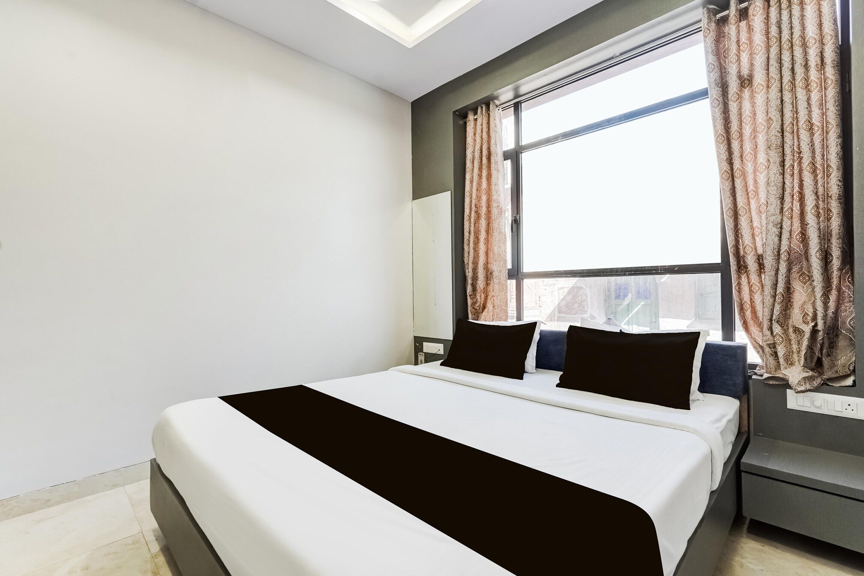 A modern hotel room with a large bed, a nightstand, a desk, and a window with curtains.