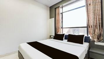 A modern hotel room with a large bed, a nightstand, a desk, and a window with curtains.