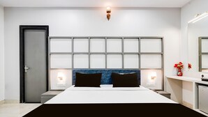 A modern hotel room with a large bed, a nightstand, a bedside table, a mirror, and a door.
