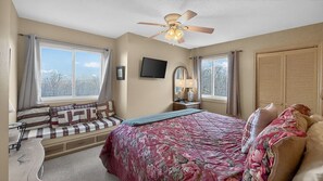 Ein Schlafzimmer mit Bett, Fensterbank, Deckenventilator, Fernseher und Kleiderschrank.