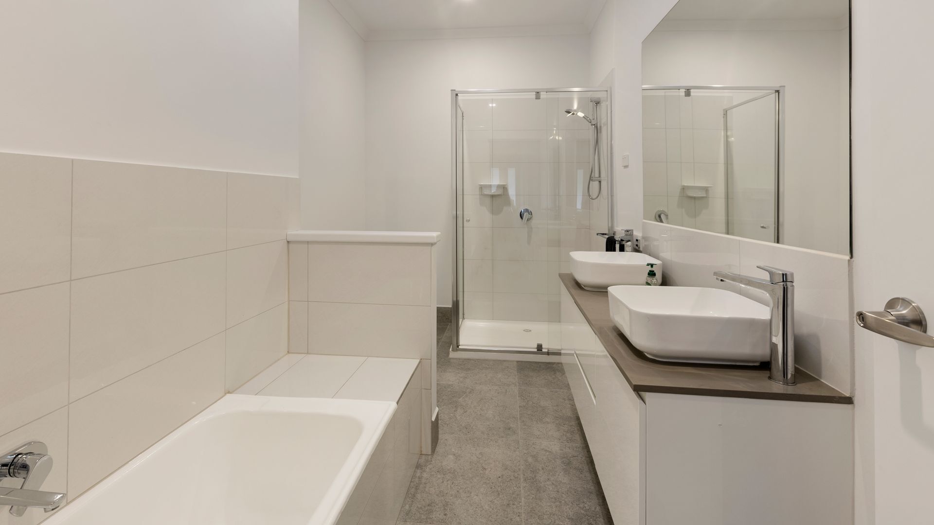 A modern bathroom with a bathtub, two sinks, a shower, and a large mirror.
