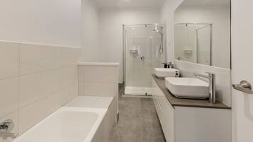 A modern bathroom with a bathtub, two sinks, a shower, and a large mirror.