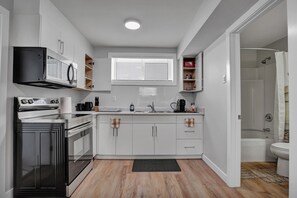 A modern kitchen with white cabinets, a built-in oven, a microwave, and a window above the sink.