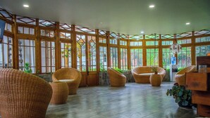 Un espacio interior amplio con mobiliario de mimbre, ventanas grandes y suelo de baldosas.